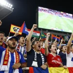 Excited football fans watching live scores on Nowgoal during a match in a vibrant stadium.