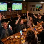 Bet on 8xbet while enjoying the live sports betting action at a vibrant sports bar with excited patrons